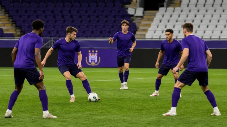 Voetballers in paarse shirts bouwen rustig op in een voetbalstadion met een discreet bord van RSC Anderlecht.