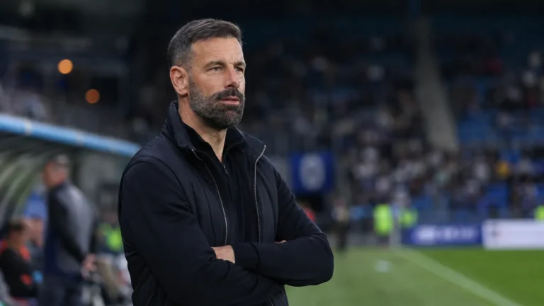 Ruud van Nistelrooij in donkere stafkleding aan de rand van een voetbalveld.