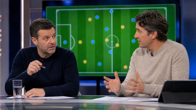 Twee analisten bespreken een voetbaltransfer aan een neutrale studiodesk.