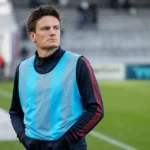 Jelle Vossen staat in een trainingshesje langs de rand van een voetbalveld.