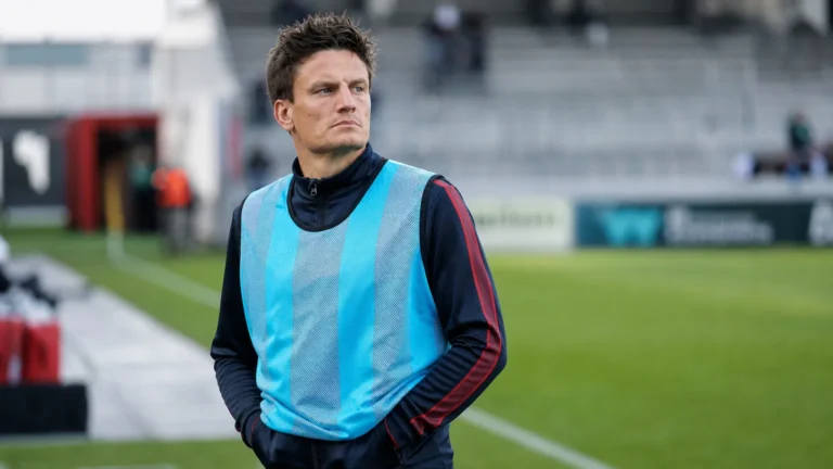 Jelle Vossen staat in een trainingshesje langs de rand van een voetbalveld.