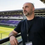 Antoine Sibierski in zwarte kleding op de tribune van het Lotto Park.
