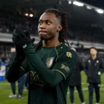 Ryan Fosso applaudisseert langs het veld in een donker wedstrijdtenue.