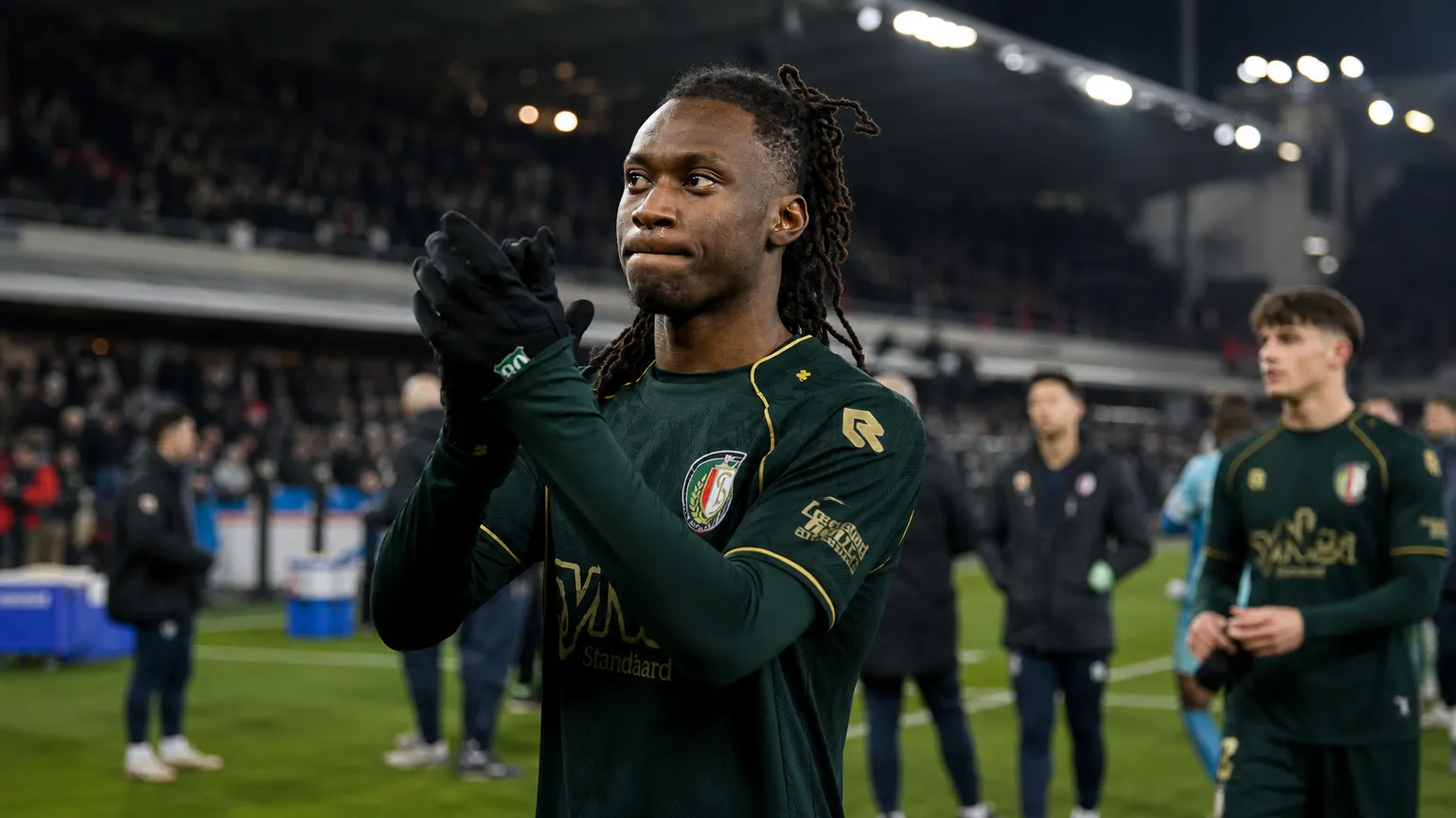 Ryan Fosso applaudisseert langs het veld in een donker wedstrijdtenue.