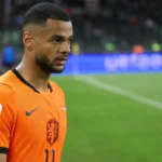 Cody Gakpo in het Nederlands elftalshirt tijdens een rustig moment langs het veld.