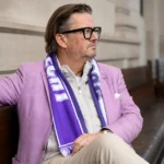 Marc Coucke zit met een paars-witte sjaal in een gerechtsgebouw.