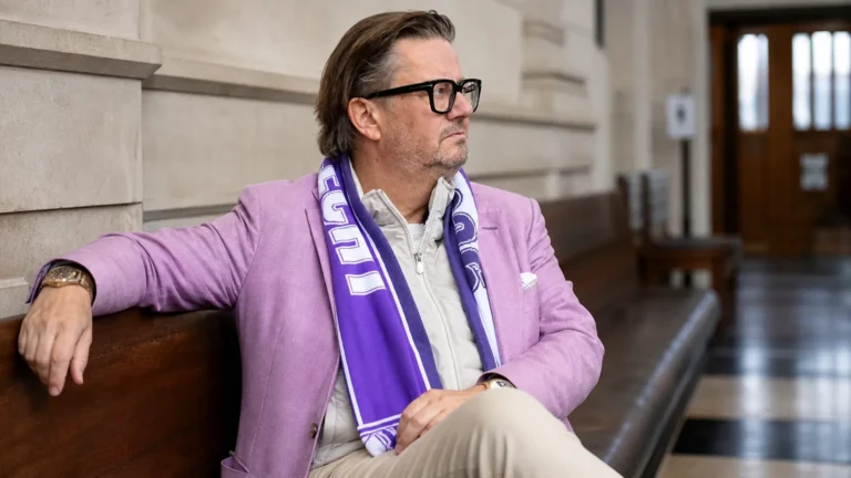 Marc Coucke zit met een paars-witte sjaal in een gerechtsgebouw.