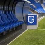 Lege technische zone langs het veld met een discreet KRC Genk-bord.