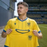 Arbnor Muja poseert met een geel STVV-shirt tijdens zijn officiële voorstelling.