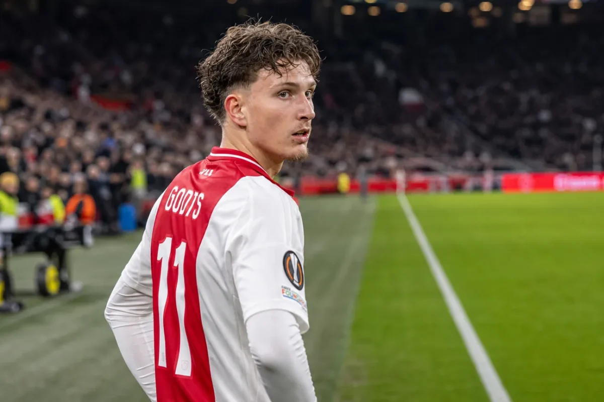 Mika Godts in het rood-witte tenue van Ajax aan de rand van het veld.