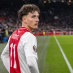 Mika Godts in het rood-witte tenue van Ajax aan de rand van het veld.