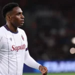 Jhon Lucumì in een wit voetbalshirt aan de rand van een verlicht veld