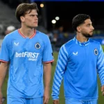 Twee spelers van Club Brugge lopen samen langs de rand van het veld.