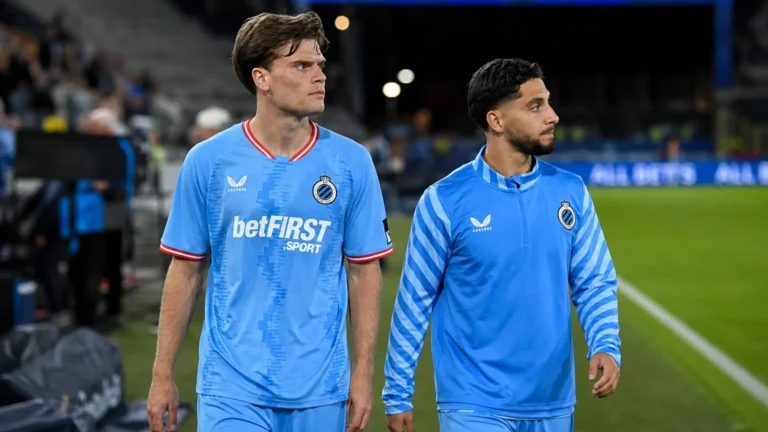 Twee spelers van Club Brugge lopen samen langs de rand van het veld.