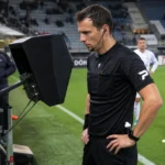 Een scheidsrechter bekijkt een fase op een Football Video Support-scherm naast het veld.