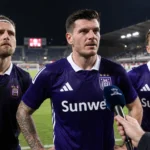 Drie Anderlecht-spelers in paarse wedstrijdkleding bij een postmatch interview aan de rand van het veld.