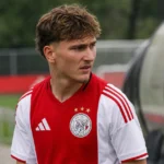 Mika Godts in een Ajax-shirt aan de rand van een voetbalveld.