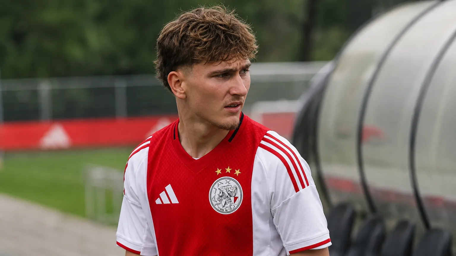 Mika Godts in een Ajax-shirt aan de rand van een voetbalveld.