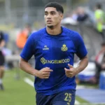 Anan Khalaili warmt op aan de rand van een voetbalveld in donkerblauw tenue.