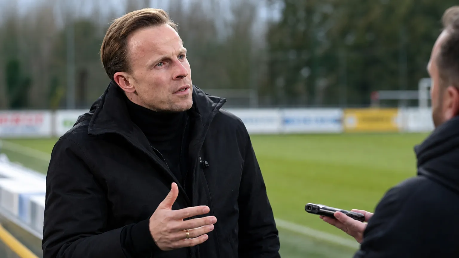 Vincent Euvrard spreekt rustig met een journalist naast het veld.