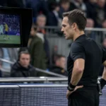 Een scheidsrechter bekijkt beelden op een videoscherm naast het voetbalveld.