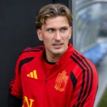 Mika Godts in een rode Belgische trainingstop in een neutrale gemengde zone naast het veld.