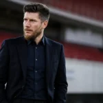 Sebastien Pocognoli in donkere formele kleding in een neutrale stadionperszone.