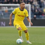 Rafik Belghali in een geel Hellas Verona-tenue op het veld in een stadion.