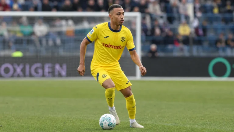 Rafik Belghali in een geel Hellas Verona-tenue op het veld in een stadion.