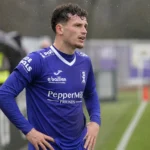 Leandro Rousseau in een blauw voetbalshirt aan de zijlijn van een veld.