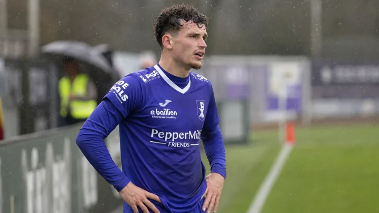 Leandro Rousseau in een blauw voetbalshirt aan de zijlijn van een veld.