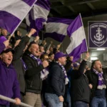 Supporters van Patro Eisden zwaaien met paars-witte vlaggen in de tribune.