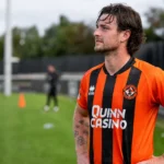 Will Ferry van Dundee United staat in zijn oranje-zwarte wedstrijdshirt naast het trainingsveld.