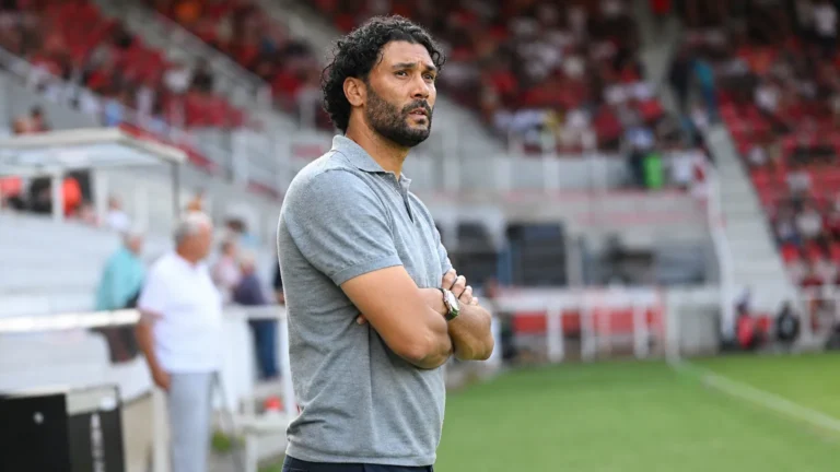 Marvin Compper staat in een grijze polo langs de zijlijn van een voetbalstadion.