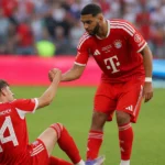 Ismael Saibari in rood Bayern-tenue helpt een zittende ploegmaat tijdens een oefenwedstrijd.