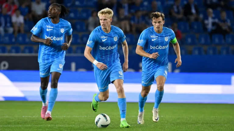 Drie spelers van KRC Genk in lichtblauwe wedstrijdtenues tijdens een competitiewedstrijd.