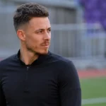 Thorgan Hazard in neutrale sportkleding langs de zijlijn van een voetbalstadion.