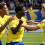 Spelers van SK Beveren vieren samen op het veld in gele shirts en blauwe shorts.