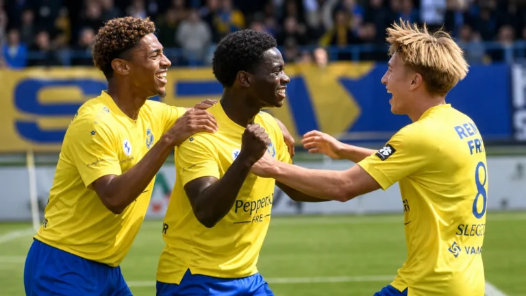 Spelers van SK Beveren vieren samen op het veld in gele shirts en blauwe shorts.