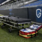 Een brancard en medische tas langs de zijlijn in een verlicht voetbalstadion.