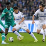 Spelers in witte en groene tenues in duel tijdens een voetbalwedstrijd.