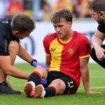 Leo Hjelde van KV Mechelen zit op het veld terwijl verzorgers hem bijstaan.