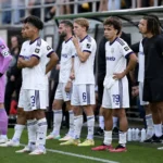 Een groep spelers van RSC Anderlecht wacht langs de zijlijn van het veld.