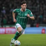 Olivier Deman in een groen gestreept voetbalshirt tijdens een actie op het veld.