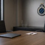 Een lege vergaderruimte van een voetbalclub met een discreet Club Brugge-embleem aan de muur.