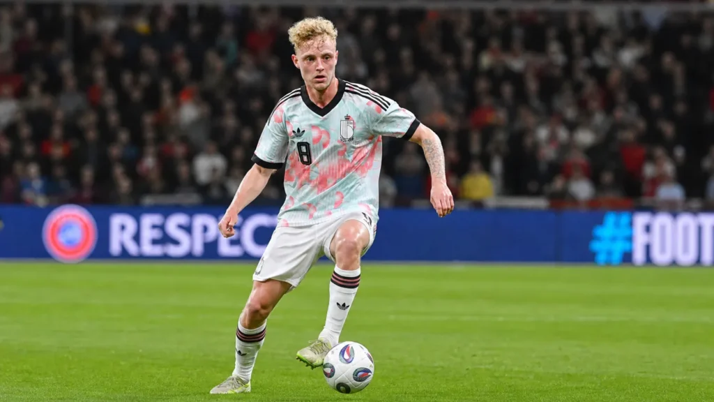 Joaquin Seys in een licht patroonshirt tijdens een actie op een verlicht voetbalveld.