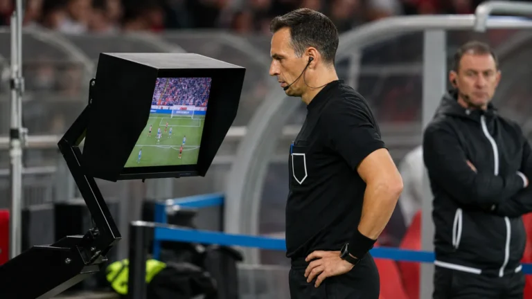 Een scheidsrechter bekijkt beelden op een VAR-monitor naast het veld.