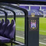 Een lege vervangersbank naast een voetbalveld met een discreet RSC Anderlecht-bord.