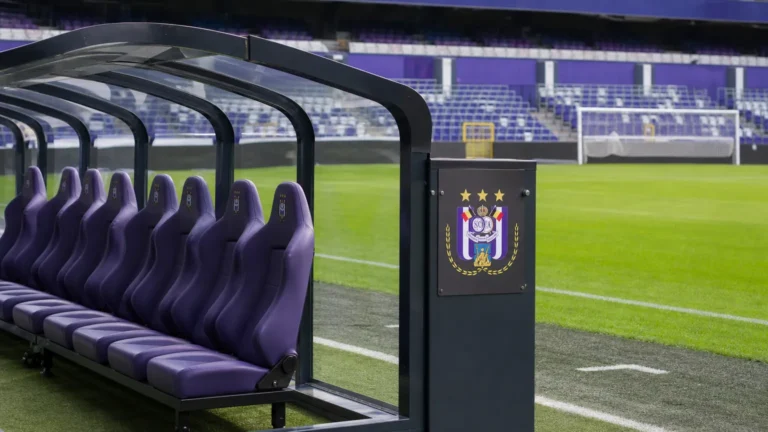 Een lege vervangersbank naast een voetbalveld met een discreet RSC Anderlecht-bord.