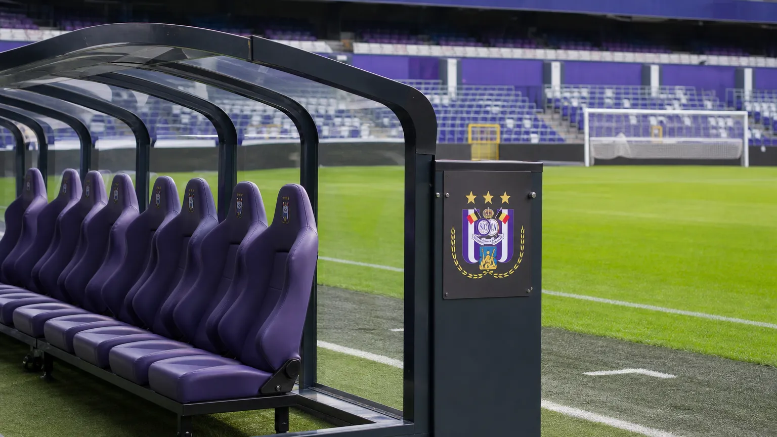 Een lege vervangersbank naast een voetbalveld met een discreet RSC Anderlecht-bord.